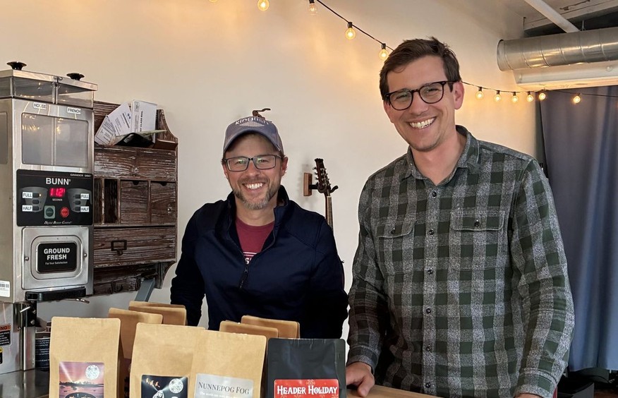 The two founders of Bond Coffee Roasters standing with bags of coffee.