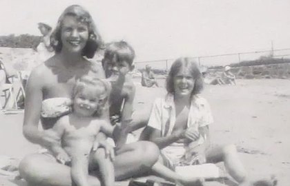 A black-and-white photograph of a young Sylvia Plath on a beach with three children.