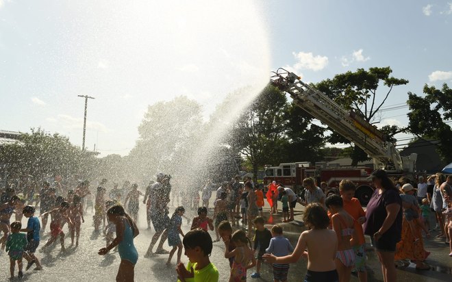 A fire department ladder truck sprays water over a street full of children.
