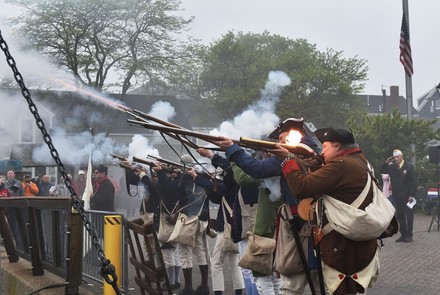 Reenactors fire a musket volley beside the harbor.