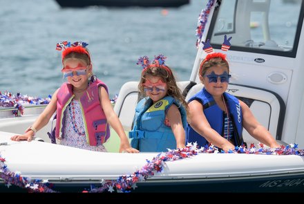 Three children in a boat decorated for the Fourth of July.