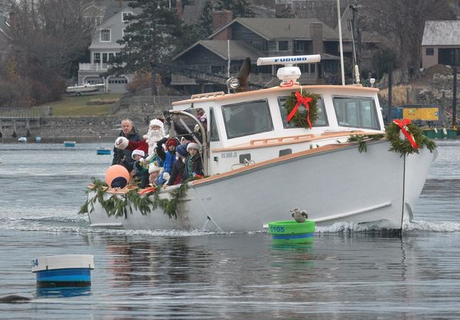 Santa arrives by lobster boat with garland on the bow.